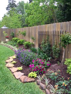 a garden with lots of plants and rocks in the center, along side a wooden fence