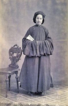 an old black and white photo of a woman standing next to a chair with a book in her hand