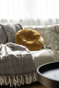 a couch with a yellow pillow on top of it next to a table and window