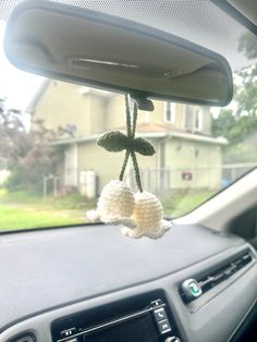 two crocheted balls hanging from the dashboard of a car, in front of a house