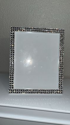 a white square frame with black and silver beading on it sitting on a shelf