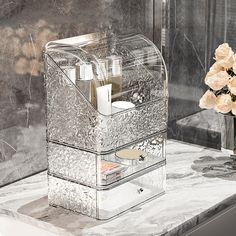 a clear box with some flowers in it on a marble table next to a mirror