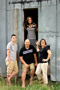 four people posing for a photo in front of an outhouse with the door open