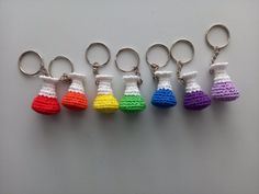 six crocheted keychains are lined up on a white surface, each with different colors