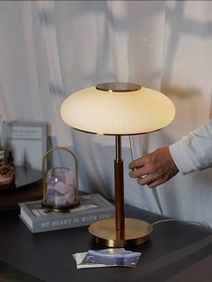 a person standing next to a table with a lamp on it's side and some books