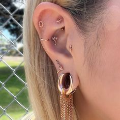 a close up of a person with ear piercings on their ears and behind them is a chain link fence