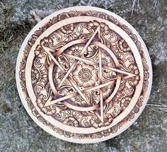 a wooden plate with a pentagramus design on it sitting on top of some rocks