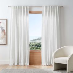 a white chair sitting in front of a window with curtains hanging on the windowsill