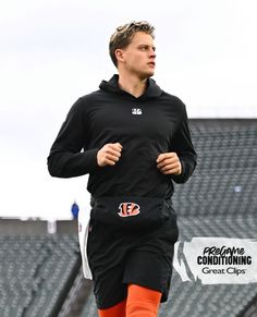 a man in black shirt and orange pants running on field with bleachers behind him