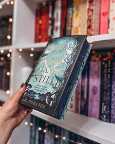 a person holding up a book in front of a bookshelf full of books