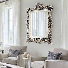 a living room filled with furniture and a large mirror on the wall above two chairs