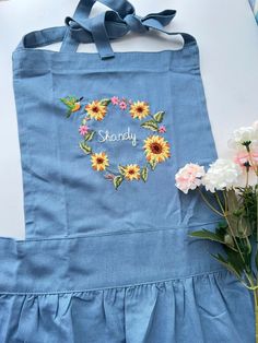 a blue apron with sunflowers and the words shandy on it next to flowers