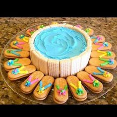 a cake with blue frosting surrounded by cookies and decorations on a glass platter