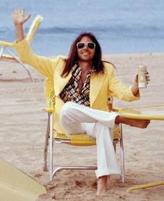 a man sitting in a chair on the beach with his arms up and legs crossed