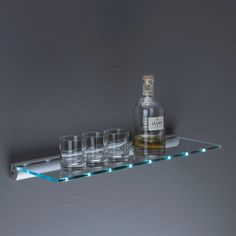 three shot glasses and a bottle on a glass shelf with light up lights around it