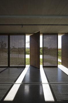 an open room with two doors and shadows on the floor, in front of a grassy area