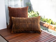 two brown leather pillows sitting on top of a wooden bench next to a glass window