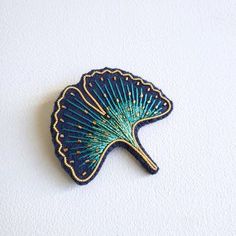 a blue and gold fan shaped brooch sitting on top of a white wall