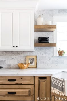 a kitchen with white cabinets and marble counter tops, black dishes on wooden shelves above the sink