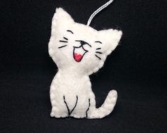 a white cat ornament hanging from a string on a black background with a red tongue