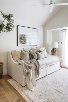 a living room with a white couch and some pillows on the floor next to a potted plant