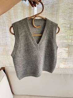 a gray sweater vest hanging on a wooden hanger in front of a white couch