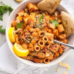 a bowl filled with pasta and lemon wedges on top of a white table cloth