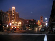 an empty city street at night with the lights on and signs lit up in the dark