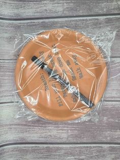 an orange frisbee wrapped in plastic on top of a wooden table next to a knife