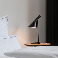 a bed with white sheets and a black lamp on it next to a wooden tray