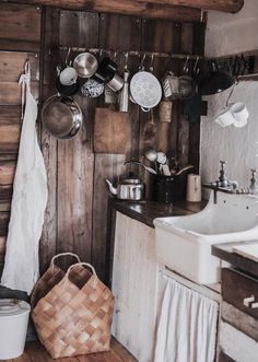 a rustic kitchen with wooden walls and white sink, hanging pots and pans on the wall