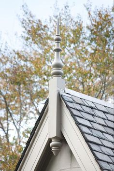 the top of a house with a clock on it's side and trees in the background