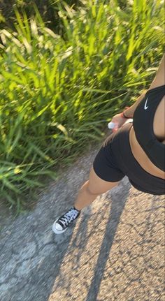 a woman walking down a street next to tall grass and bushes with her cell phone in her hand