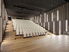 an empty auditorium with rows of white chairs and wood flooring, along with wooden slats on the walls