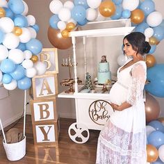 a pregnant woman standing in front of a cake stand with balloons and decorations on it