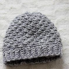 a gray and white crocheted hat laying on top of a bed next to a pillow