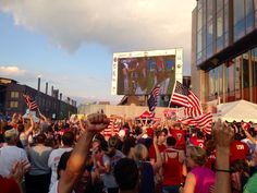 a crowd of people holding american flags in front of a large screen on the side of a building