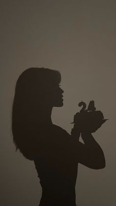 the silhouette of a woman holding a bird in her hand, against a gray background