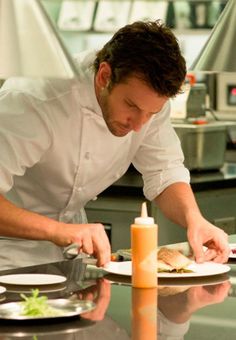 a man is preparing food in a kitchen with candles on the table and plates around him