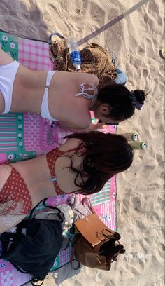 two women in bathing suits sitting on a towel at the beach with their feet up