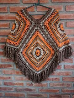 an orange and brown crocheted shawl hanging on a brick wall next to a brick wall