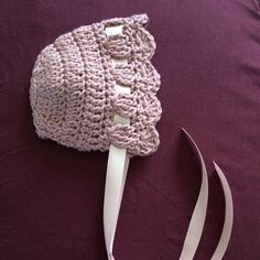 a crocheted hat with white ribbon on a purple blanket next to a pair of scissors