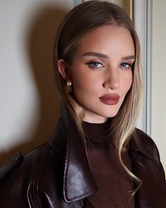 a woman with blonde hair wearing a brown leather jacket and gold hoop earrings is looking at the camera