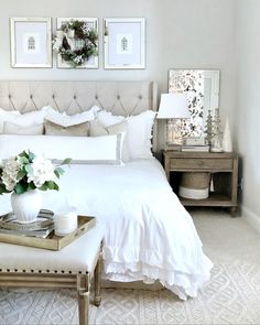 a bedroom with white bedding and pictures on the wall above it, along with a tray full of flowers