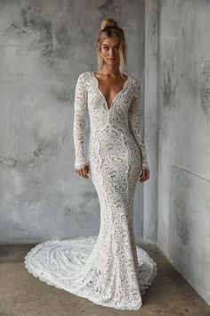 a woman in a long sleeved wedding dress standing against a wall with her hands on her hips