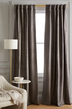 a living room with a chair, lamp and curtains in grey colors on the windowsill