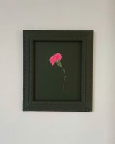 a pink flower in a black frame on the wall