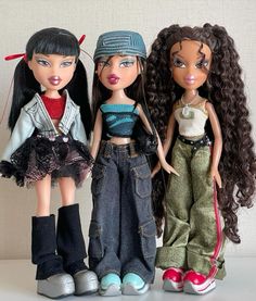 three dolls standing next to each other in front of a white wall and one is wearing jeans