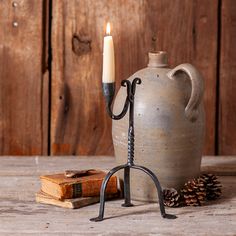 a candle is lit in front of a stone jug with a hook on the handle