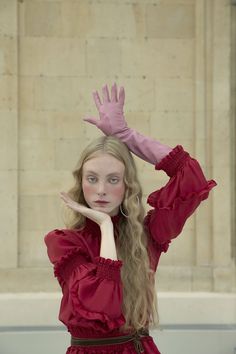 a woman with long blonde hair wearing pink gloves and holding her hands up in the air